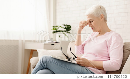 Eye strain problem. Upset senior woman taking off glasses, suffering from blurry vision after long using of digital tablet, free space Eye strain problem. Upset senior woman taking off glasses, suffering from blurry vision after long using of digital tablet, free space 114700320