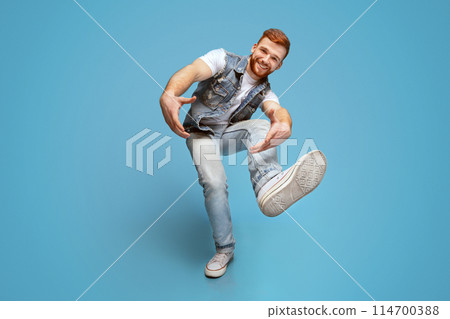 Come on. Smiling millennial caucasian guy, fool around and marked out with hands at camera, full length, blue studio background. 114700388