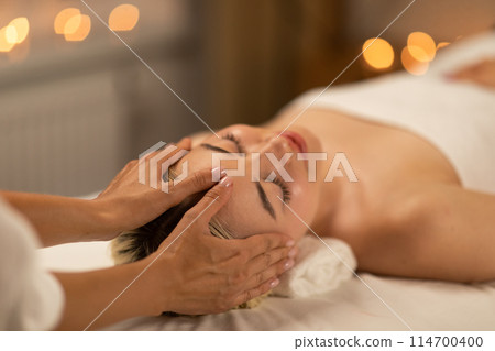 A calming scene at a spa with a young blonde woman receiving a delicate facial massage, showcasing her relaxed demeanor and comfort. 114700400