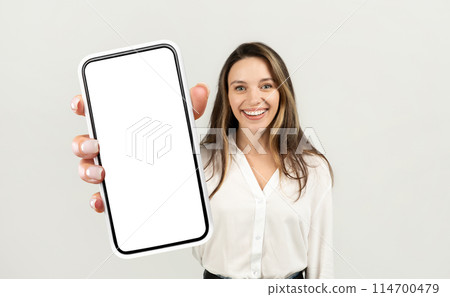 A woman entrepreneur holding a cell phone up in front of her with a blank screen visible. She appears to be examining the phone closely, possibly checking for notifications or composing a message. 114700479