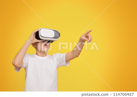 Wow, its amazing. Boy experiencing virtual reality, gesturing on orange studio background, copy space 114700487