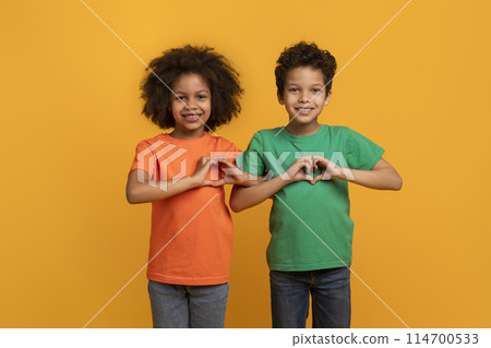 Happy African American kids boy and girl showing heart shape gestures over chest and smiling at camera, isolated on yellow studio background 114700533