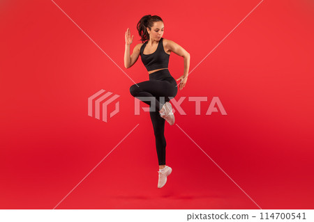 A woman dressed in a black sports bra top and black leggings is engaged in a workout routine. She is focused and determined while performing physical exercises to maintain fitness and strength. 114700541