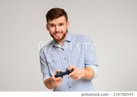 Gambling addiction. Young guy holding joystick and playing video games on studio background, panorama, copy space 114700545