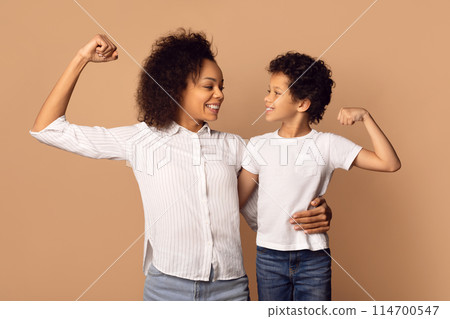 African American woman and a boy are standing next to each other, showing biceps and smiling, isolated on beige background 114700547