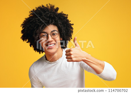 I like it. Cheerful african-american curly guy showing thumb up and smiling at camera, orange background 114700702