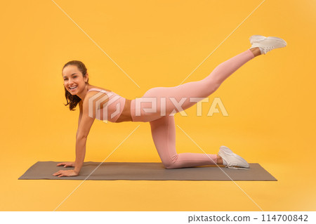 A woman dressed in pink clothing is actively engaging in a yoga pose, showcasing flexibility and strength. She holds the pose with poise and focus, demonstrating balance and concentration. A woman dressed in pink clothing is actively engaging in a yoga pose, showcasing flexibility and strength. She holds the pose with poise and focus, demonstrating balance and concentration. 114700842