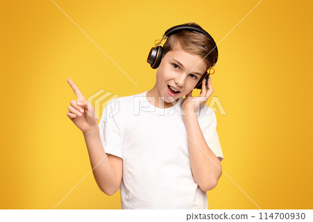 A young boy with headphones on, raising his hand to make a peace sign. A young boy with headphones on, raising his hand to make a peace sign. 114700930