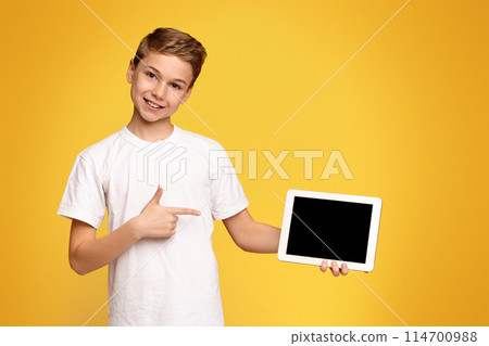 A young male child is seen holding a tablet computer in his hands. 114700988