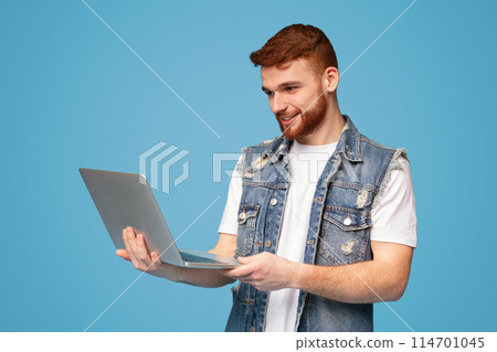 Smiling millennial redhaired man having video conversation on laptop on blue studio background, copy space Smiling millennial redhaired man having video conversation on laptop on blue studio background, copy space 114701045