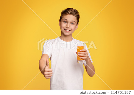 Strengthen immunity. Cool teenager with orange juice gesturing thumb up, studio background Strengthen immunity. Cool teenager with orange juice gesturing thumb up, studio background 114701197