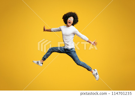 Go, man. Hurry up. Emotional black guy jumping in air, walking on orange studio background 114701235