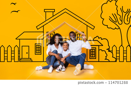 Happy African American family of three father mother and daughter sitting on floor over illustrated house of their dreams over yellow wall background, parents holding a roof 114701288