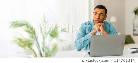 A thoughtful african american man working from home with a laptop, pen, and notepad, plus ample copy space for a web-banner 114701314