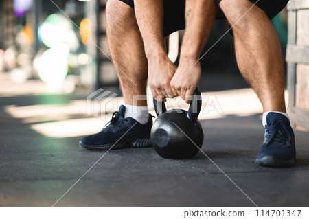 Cropped of man is bending over while holding a kettle in his hand, have workout session at modern gym, closeup, copy space 114701347