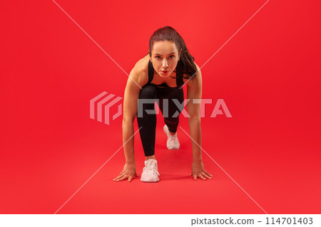 A woman dressed in black clothing is executing a handstand position, balancing on her hands with legs extended upwards, red studio background 114701403