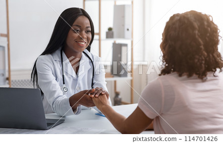 African cheerful female doctor holding patient hand, consultation at clinic 114701426