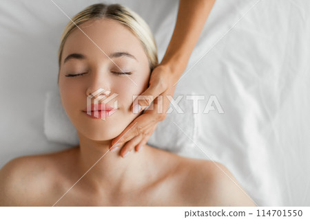 A blissful young woman is receiving a soothing neck massage from a therapists skilled hands, evoking a sense of tranquility and wellness, copy space, top view A blissful young woman is receiving a soothing neck massage from a therapists skilled hands, evoking a sense of tranquility and wellness, copy space, top view 114701550
