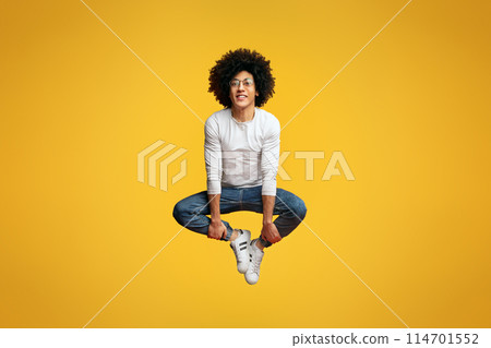 Levitation. Joyful curly african-american man jumping, sitting in air on orange studio background Levitation. Joyful curly african-american man jumping, sitting in air on orange studio background 114701552