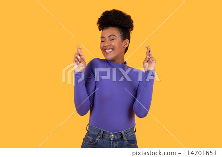 Hispanic woman wearing a purple shirt is gesturing with her hand in a clear and deliberate manner, cross fingers. Her expression is focused, indicating intent behind the gesture she is making. Hispanic woman wearing a purple shirt is gesturing with her hand in a clear and deliberate manner, cross fingers. Her expression is focused, indicating intent behind the gesture she is making. 114701651