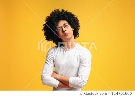 Skeptical black millennial man, looking suspiciously at camera with crossed hands, orange background Skeptical black millennial man, looking suspiciously at camera with crossed hands, orange background 114701660