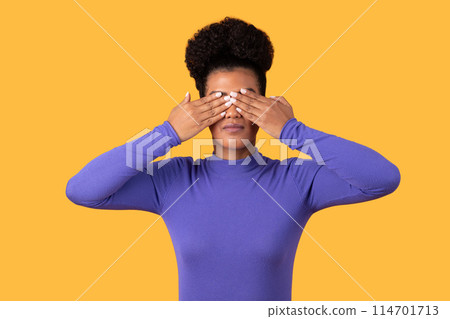 A woman is shown covering her eyes with her hands in this straightforward image. She appears to be blocking out light or shielding her eyes from something. 114701713