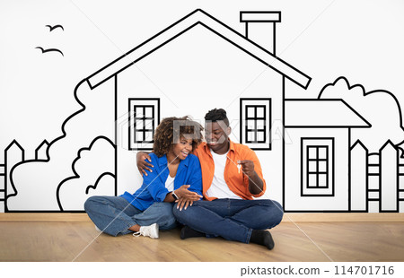 Cheerful young African American couple sitting by white wall with a house outline, dreaming of a home, holding key. Real estate, mortgage concept Cheerful young African American couple sitting by white wall with a house outline, dreaming of a home, holding key. Real estate, mortgage concept 114701716