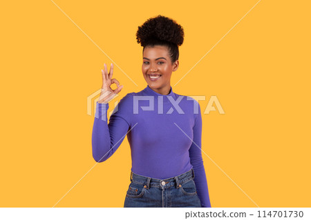 Hispanic woman wearing a purple shirt is standing and making okay gesture with her hand, isolated on yellow background Hispanic woman wearing a purple shirt is standing and making okay gesture with her hand, isolated on yellow background 114701730