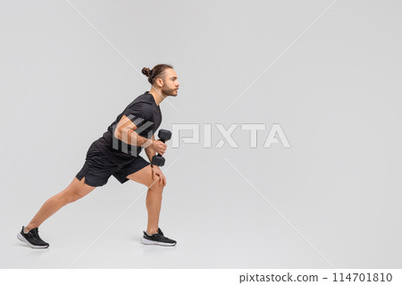 A man, wearing a black shirt and shorts, is shown holding a dumbbell in his hand. He appears to be engaged in weightlifting or strength training, copy space 114701810