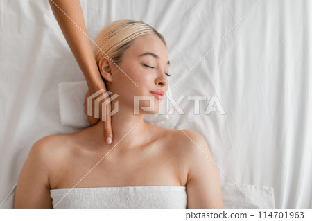 A woman laying on a massage table, receiving a neck massage from a therapist at a spa. The therapist is using gentle pressure and kneading motions to relax the muscles, top view, copy space 114701963