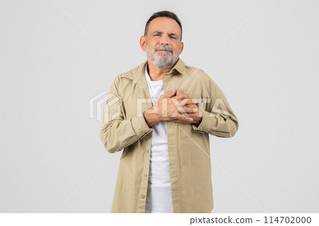 A senior man is standing upright with his hands neatly folded in front of his chest, experiencing heart attack on white background 114702000