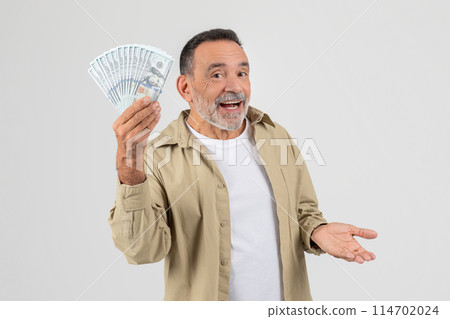 A senior man standing while holding a large amount of cash in his hand. The money is visible and neatly arranged in the mans grasp, indicating wealth or financial success. 114702024