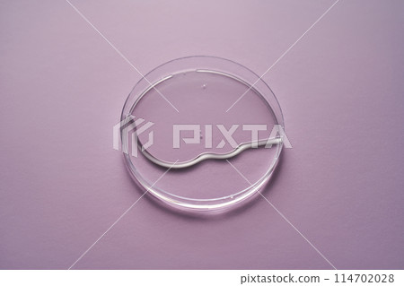 Serum or cosmetic oil flows into a transparent bowl on a purple background. 114702028