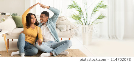 African American couple creating a house shape with hands, emphasizing togetherness, with ample copy space and web-banner layout 114702078