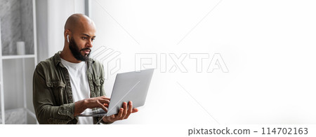 An african american man is deeply concentrated while working on his laptop on a clean background with copy space for a web-banner 114702163