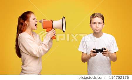 Mother shouting through megaphone at boy playing with joystick, orange studio background Mother shouting through megaphone at boy playing with joystick, orange studio background 114702176