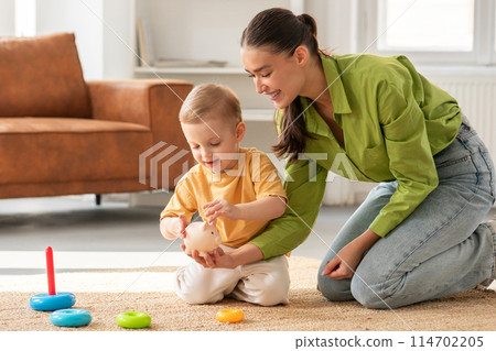 A woman dressed in casual clothing is sitting on the floor, engaging with a young child. Kid appears to be enjoying the interaction with mother, with toys scattered around them. 114702205