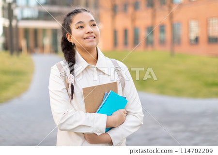 A girl wearing a white shirt is standing while holding a folder in her hands. She appears focused and determined as she looks at copy space 114702209