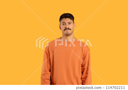 Confused man with a mustache stands in front of a vibrant yellow background, his expression neutral. 114702211