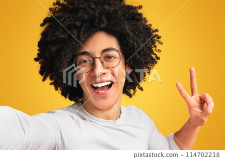 Selfie time. Cheerful african american guy gesturing v sign on camera, orange background 114702218