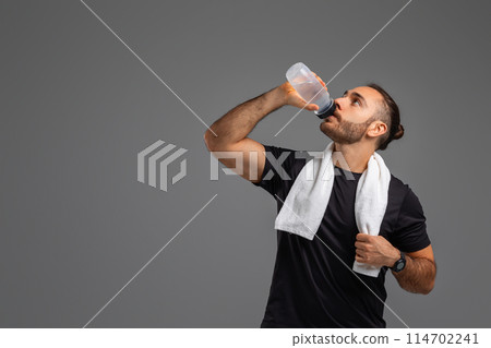 A man is shown taking a drink from a plastic water bottle. He is holding the bottle with one hand and tilting it towards his mouth to hydrate himself, copy space A man is shown taking a drink from a plastic water bottle. He is holding the bottle with one hand and tilting it towards his mouth to hydrate himself, copy space 114702241