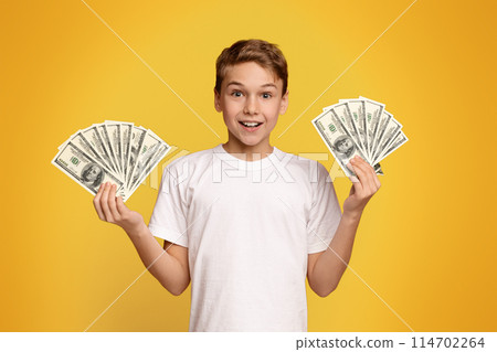 A young boy tightly grips two stacks of money in his hands, showing a sense of achievement and success. A young boy tightly grips two stacks of money in his hands, showing a sense of achievement and success. 114702264