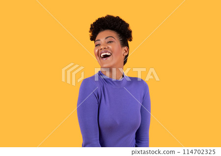 Hispanic jovial woman stands in front of a vibrant yellow background, expressing laughter. The lady body language conveys happiness and joy as she laughs heartily. Hispanic jovial woman stands in front of a vibrant yellow background, expressing laughter. The lady body language conveys happiness and joy as she laughs heartily. 114702325
