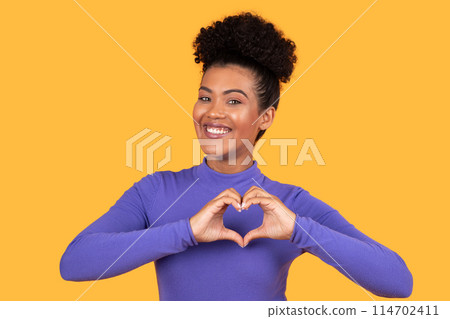 Latin woman is forming a heart shape with her hands, symbolizing love or affection. Her hands are positioned in a heart outline in front of her chest 114702411