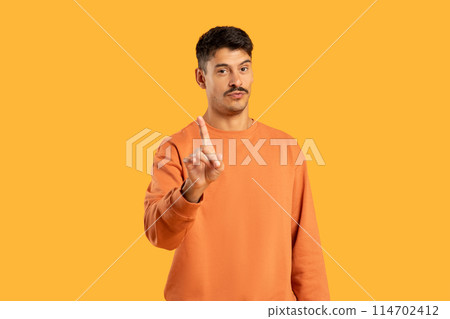 A man wearing an orange sweater is pointing at an unknown object or direction. He appears engaged and focused on the target, possibly indicating something of interest or importance. 114702412