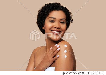A woman is shown applying a large amount of cream onto her arm. The cream appears thick and white, covering her skin completely, beige background 114702418