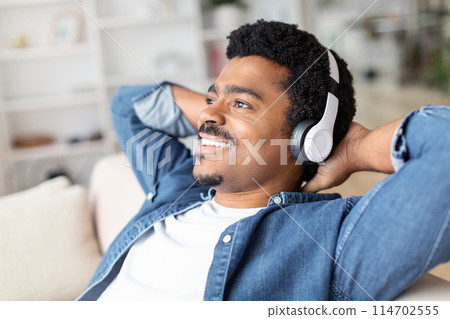 Capturing a moment of joy, an African American guy indulges in music at home, wearing headphones for intimate experience with his favorite melodies 114702555