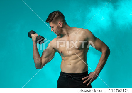 A man with no shirt is shown holding a dumbbell in a gym setting. He appears focused and exerting effort in his workout routine, showcasing strength and determination. A man with no shirt is shown holding a dumbbell in a gym setting. He appears focused and exerting effort in his workout routine, showcasing strength and determination. 114702574