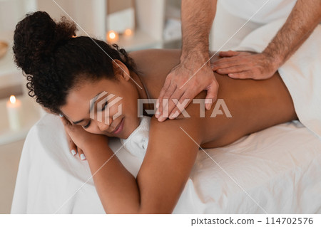 A therapist meticulously works on an african american lady's shoulder at a spa, concentrating on relieving tension in a people-focused image A therapist meticulously works on an african american lady's shoulder at a spa, concentrating on relieving tension in a people-focused image 114702576