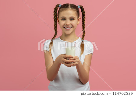 Teen girl holds a glass of milk, smiling pleasantly, isolated on a pink background, portraying a healthy lifestyle concept Teen girl holds a glass of milk, smiling pleasantly, isolated on a pink background, portraying a healthy lifestyle concept 114702589